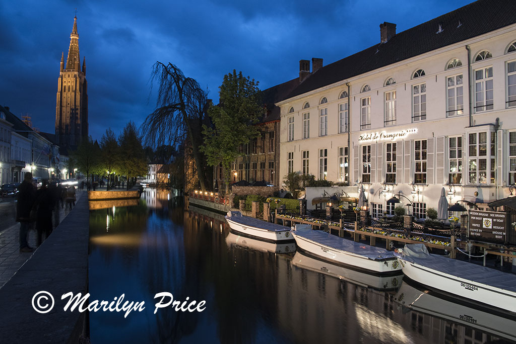 Buildings and boats reflected in a canal at twilight with the tower of the Church of Our Lady, Bruges, Belgium