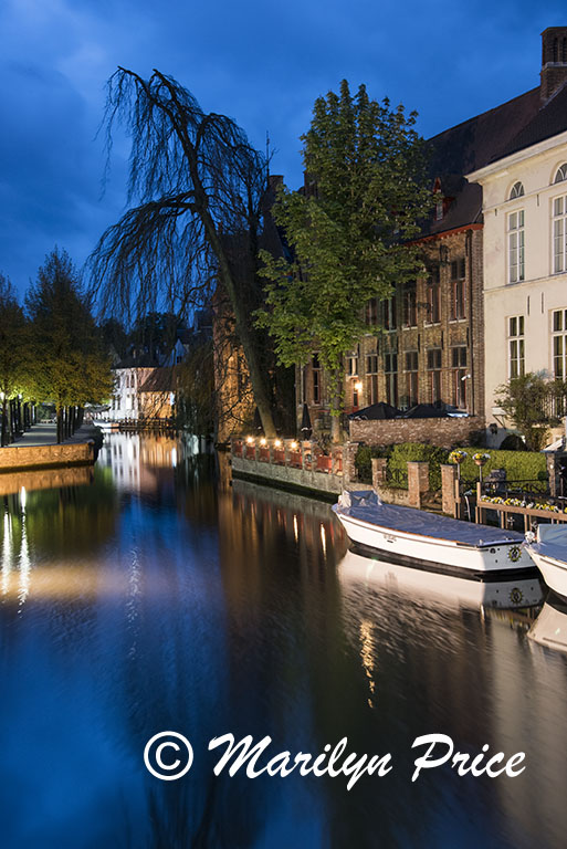 Buildings and boats reflected in a canal at twilight with the tower of the Church of Our Lady, Bruges, Belgium