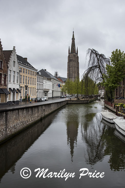 Buildings and boats reflected in a canal with the tower of the Church of Our Lady, Bruges, Belgium