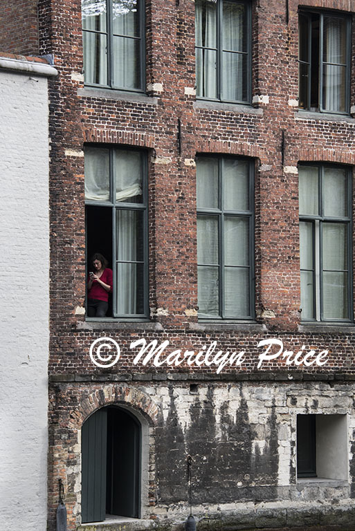 Woman texting in an open window, Bruges, Belgium