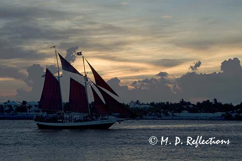 Sailboat with red sails crosses the sunset, Mallory Square, Key West, FL