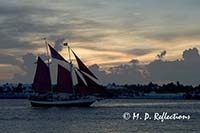 Sailboat with red sails crosses the sunset, Mallory Square, Key West, FL